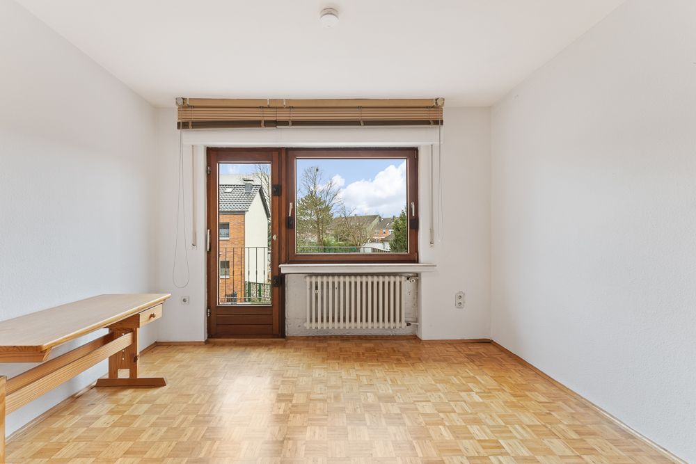 Helles Zimmer mit Parkettboden, großem Fenster, Tür zum Balkon und Holzbank an der Wand.