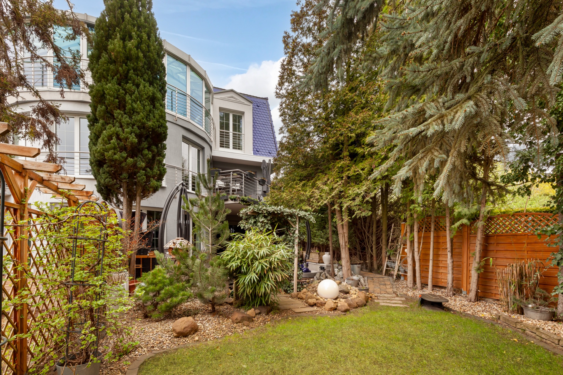 Garten mit Bäumen, Pflanzen, Rasenfläche und modernem Wohnhaus im Hintergrund.