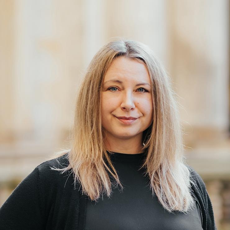 Frau mit langen blonden Haaren und schwarzer Kleidung steht draußen.