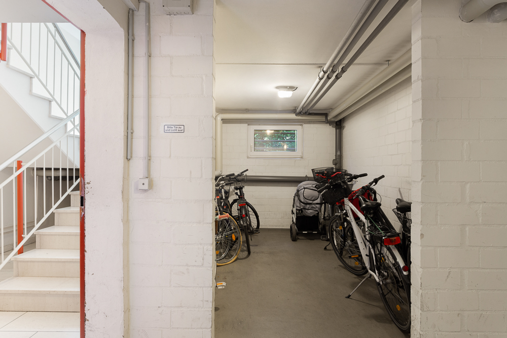 Fahrradkeller mit mehreren Fahrrädern und einem Kinderwagen, links Treppenhaus.