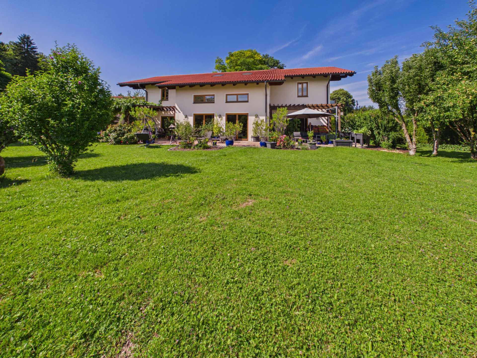 Zweistöckiges Haus mit rotem Dach und großem Garten mit viel Rasen und Bäumen.