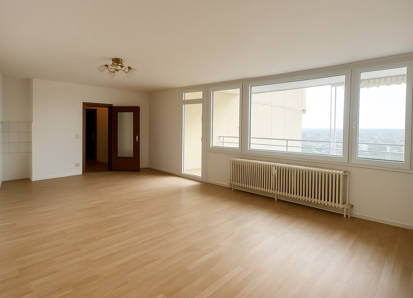 Heller leerer Raum mit Holzfußboden, großen Fenstern und Heizkörper unter dem Fenster.