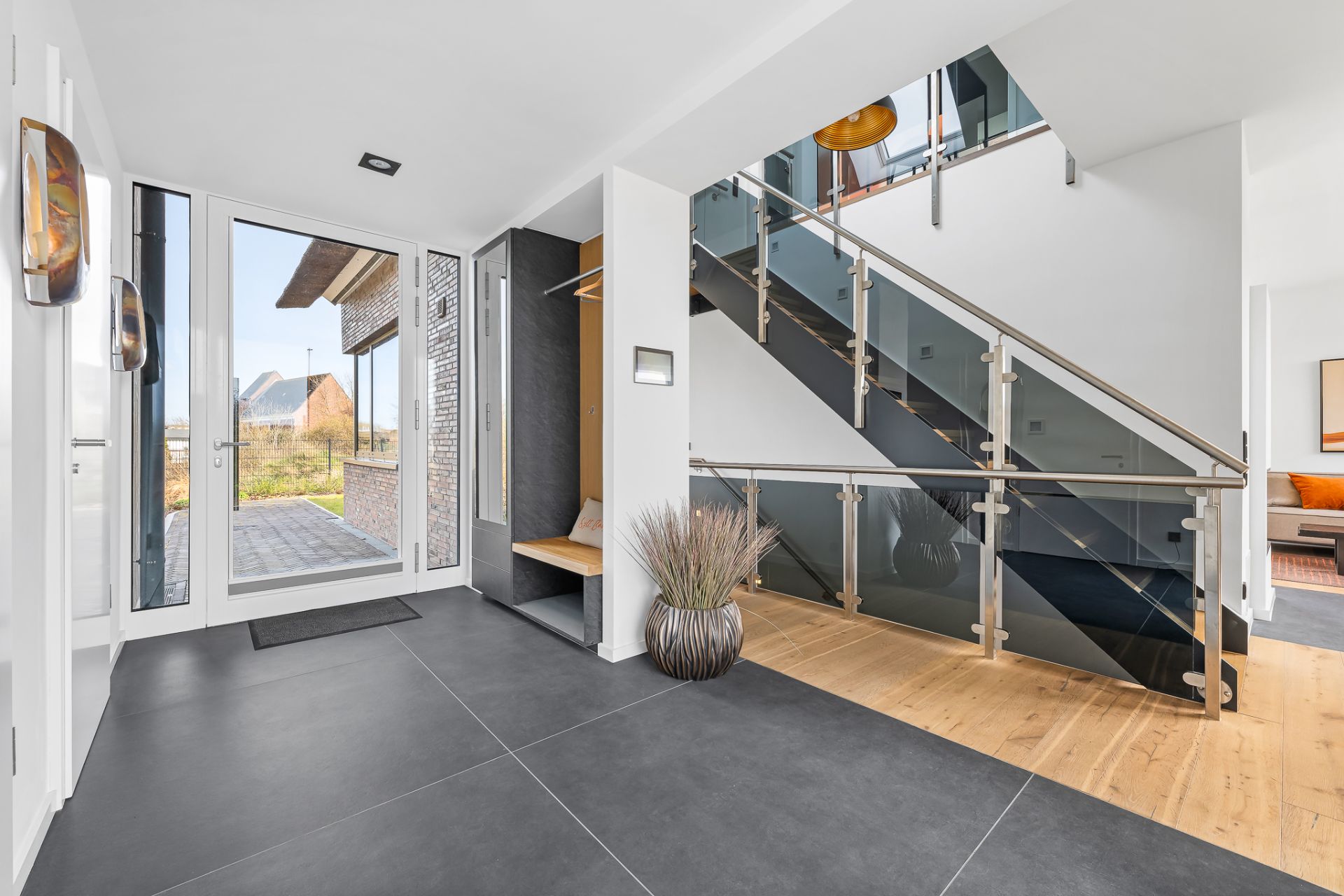 Heller Eingangsbereich mit großer Glasfront, moderner Treppe und Sitzbank.