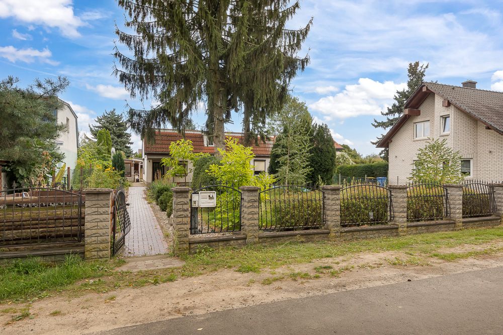 Vorgarten mit Zaun, großer Baum und zwei Wohnhäusern im Hintergrund.