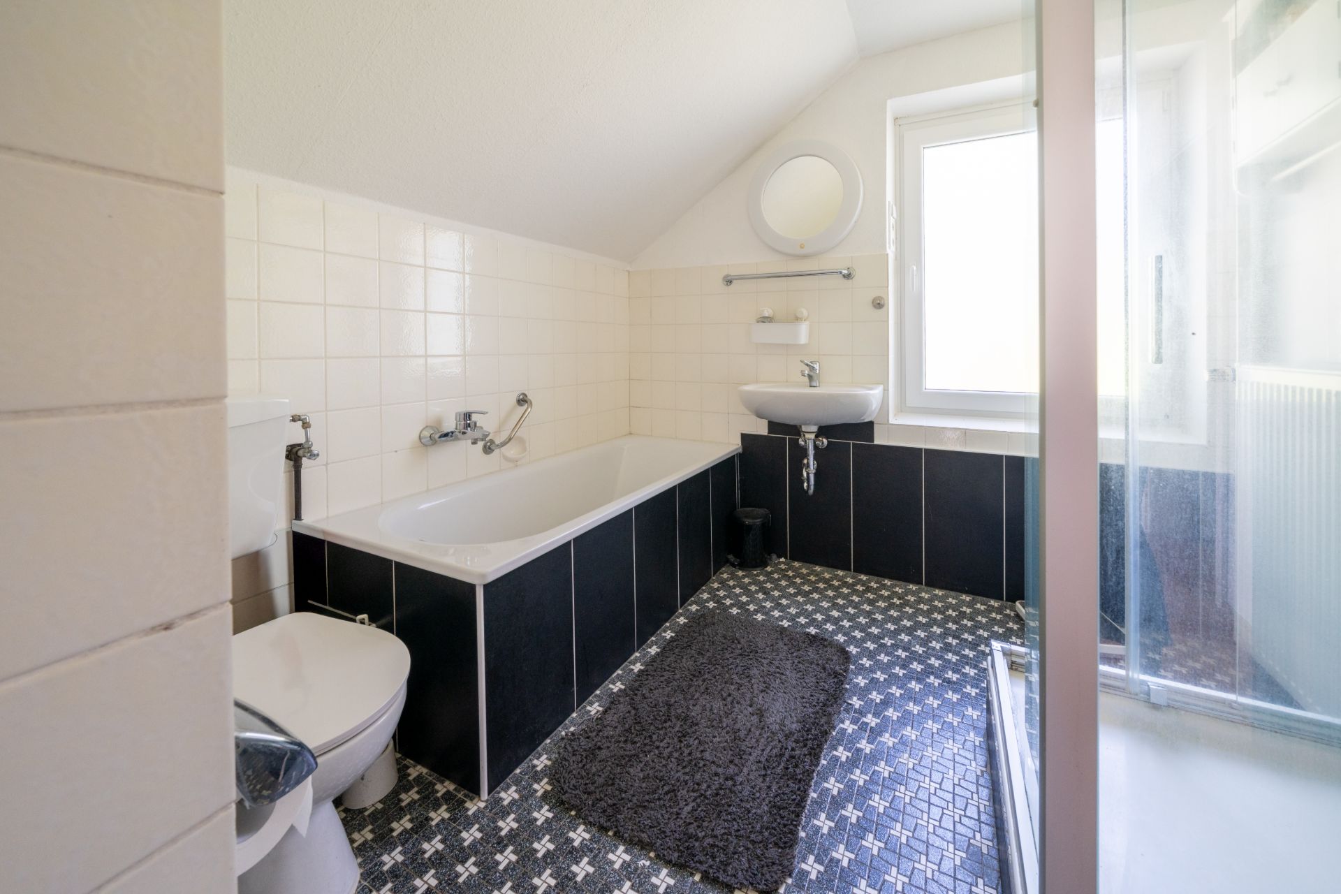 Helles Badezimmer mit Badewanne, Toilette, Waschbecken, Spiegel, Dusche und Fenster.