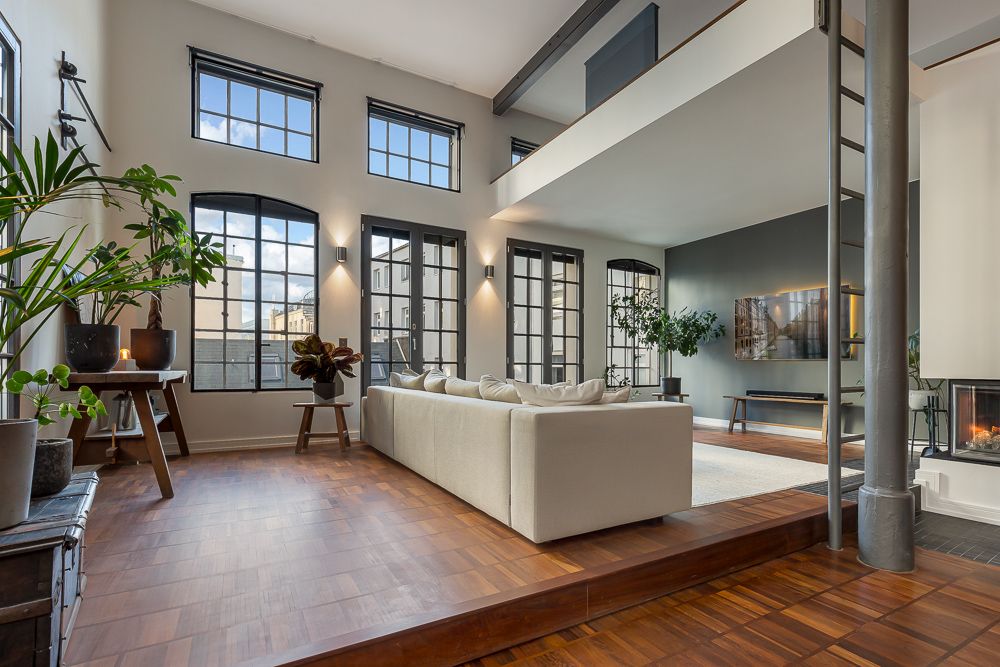 Modernes Wohnzimmer mit großen Fenstern, Holzfußboden, weißen Sofa und grünen Pflanzen.