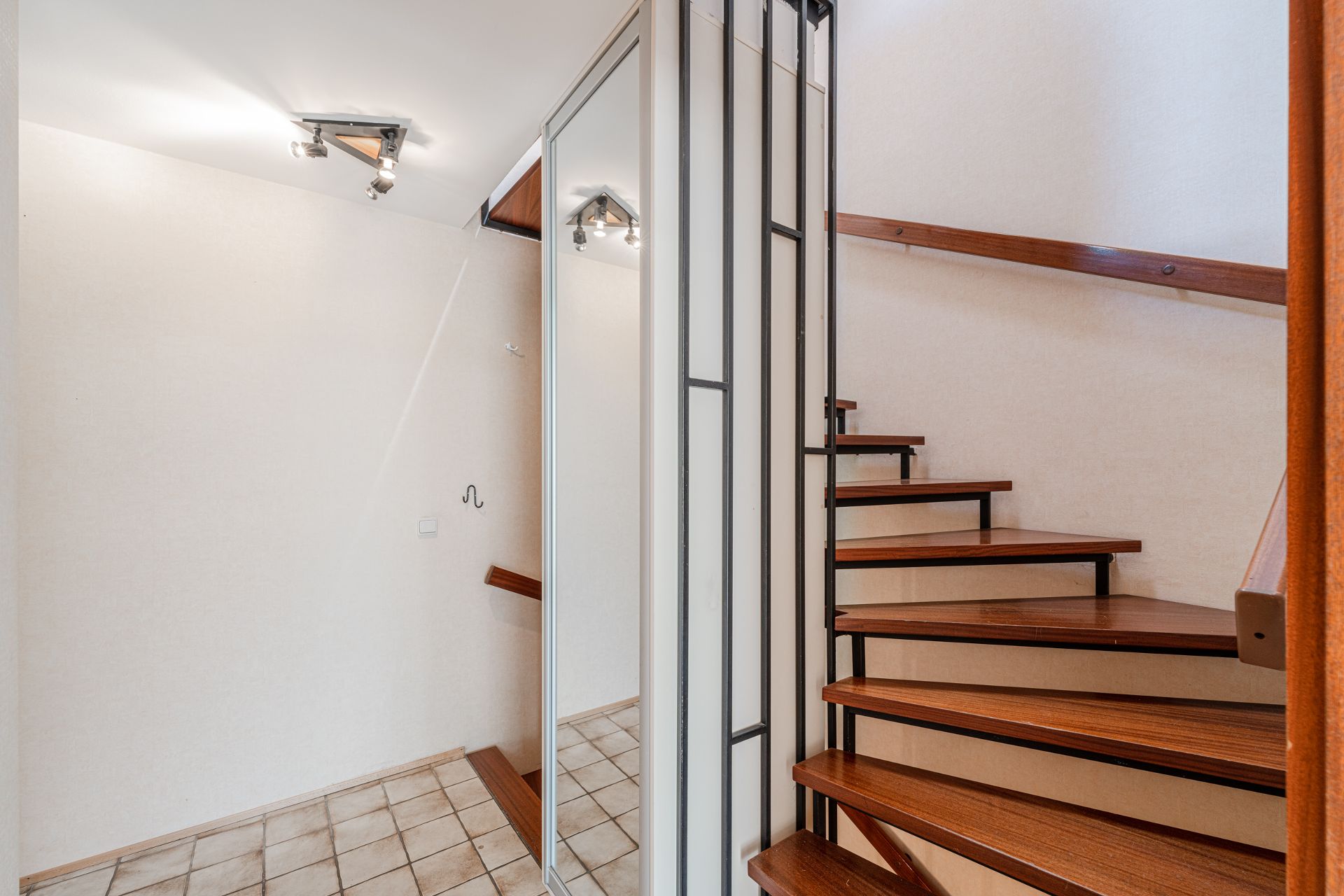 Heller Flur mit Spiegel, Fliesenboden und offener Holztreppe.