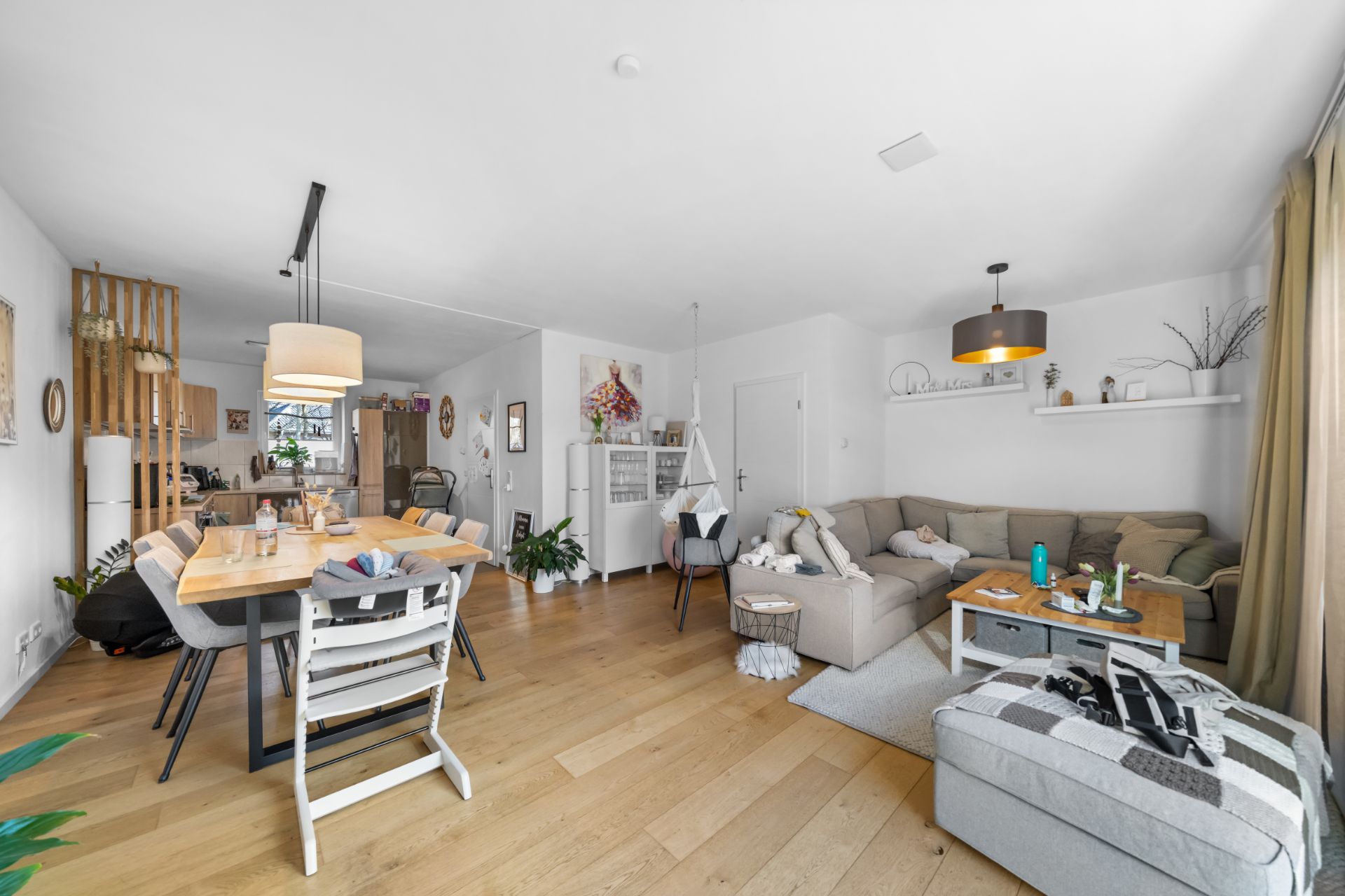 Modernes Wohnzimmer mit Ecksofa, Esstisch, Holzfußboden und großen Fenstern.