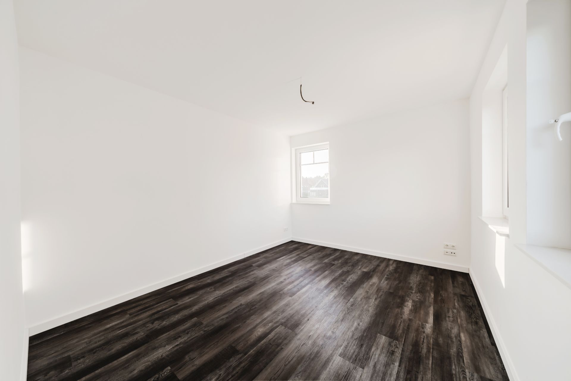 Leerer, heller Raum mit weiß gestrichenen Wänden und dunklem Holzboden, Fenster auf zwei Seiten.
