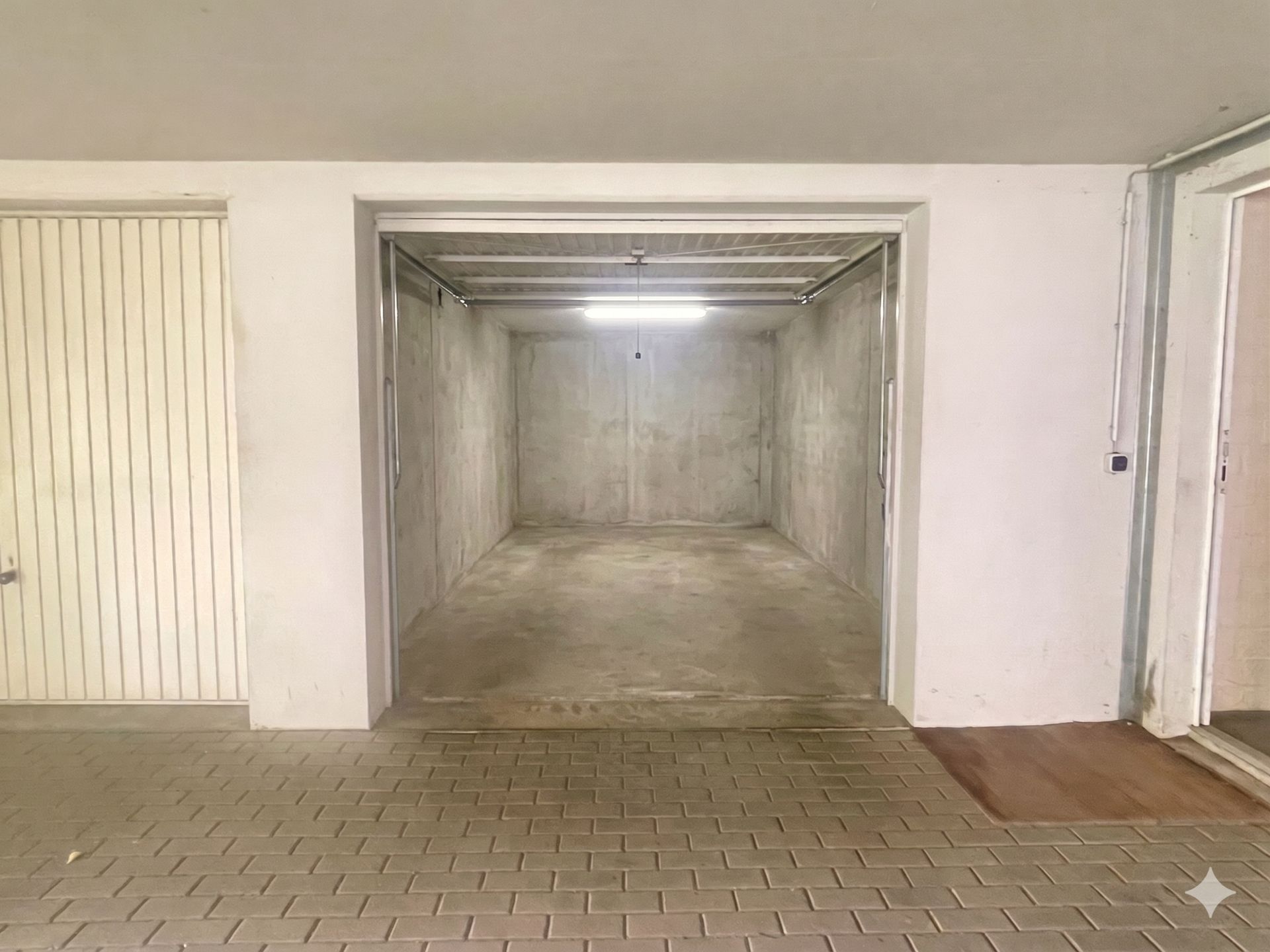 Leere Garage mit Betonwänden und offenem Tor, beleuchtet von einer Deckenlampe.