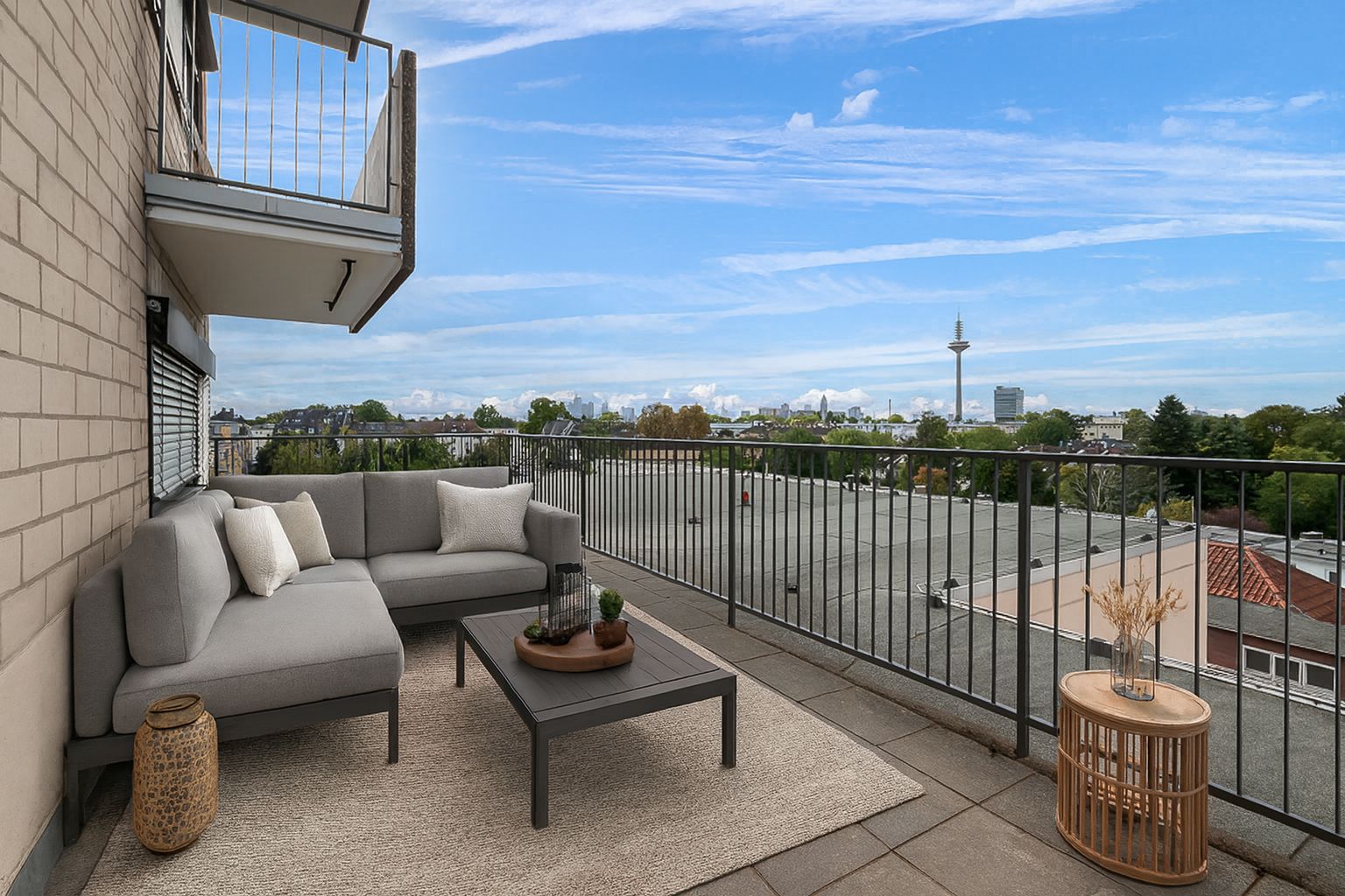 Balkon mit Sitzgruppe, Couchtisch, Teppich und Stadtblick bei blauem Himmel.