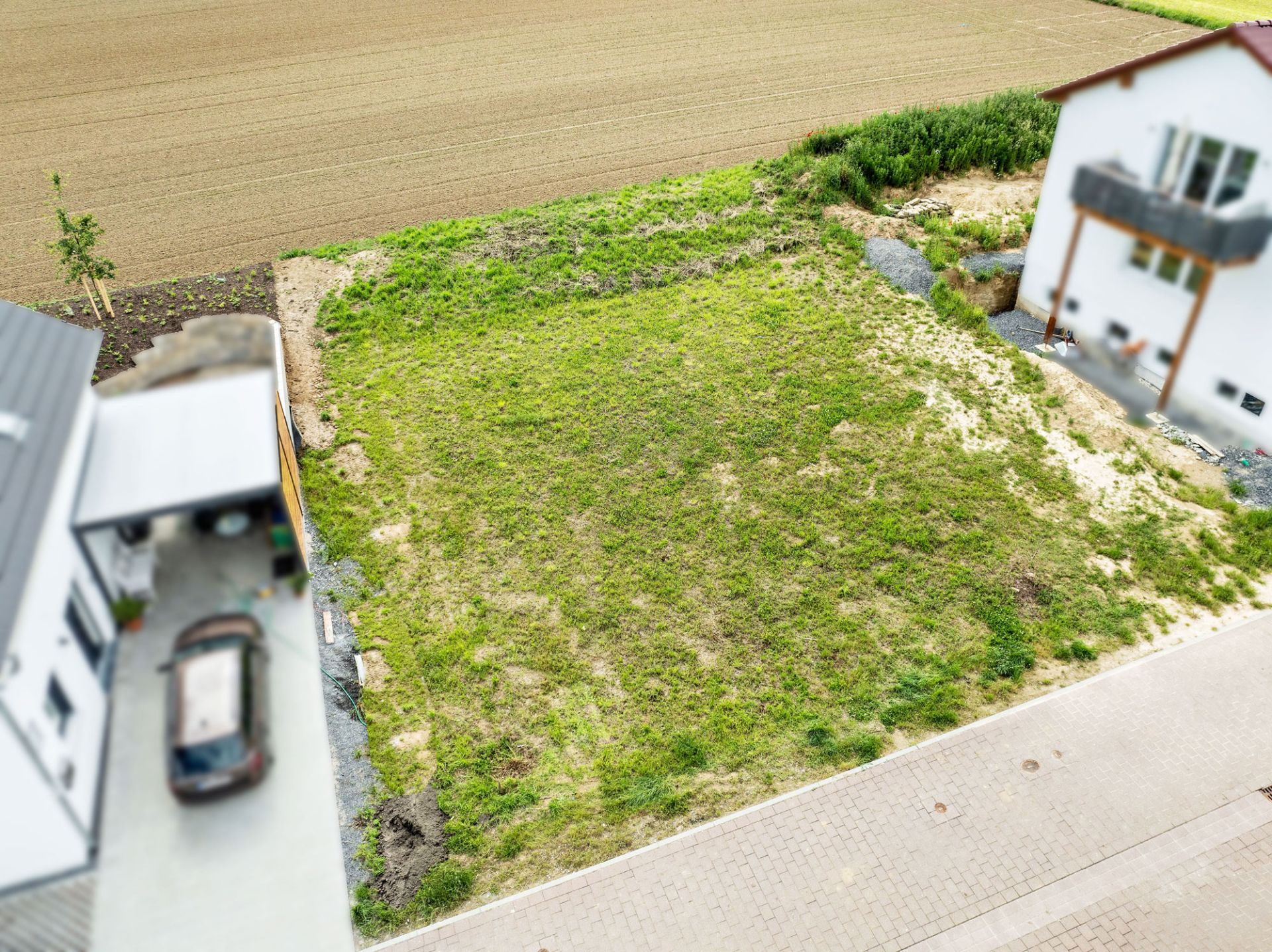Grünes, leeres Grundstück zwischen zwei Wohnhäusern an einer gepflasterten Straße.