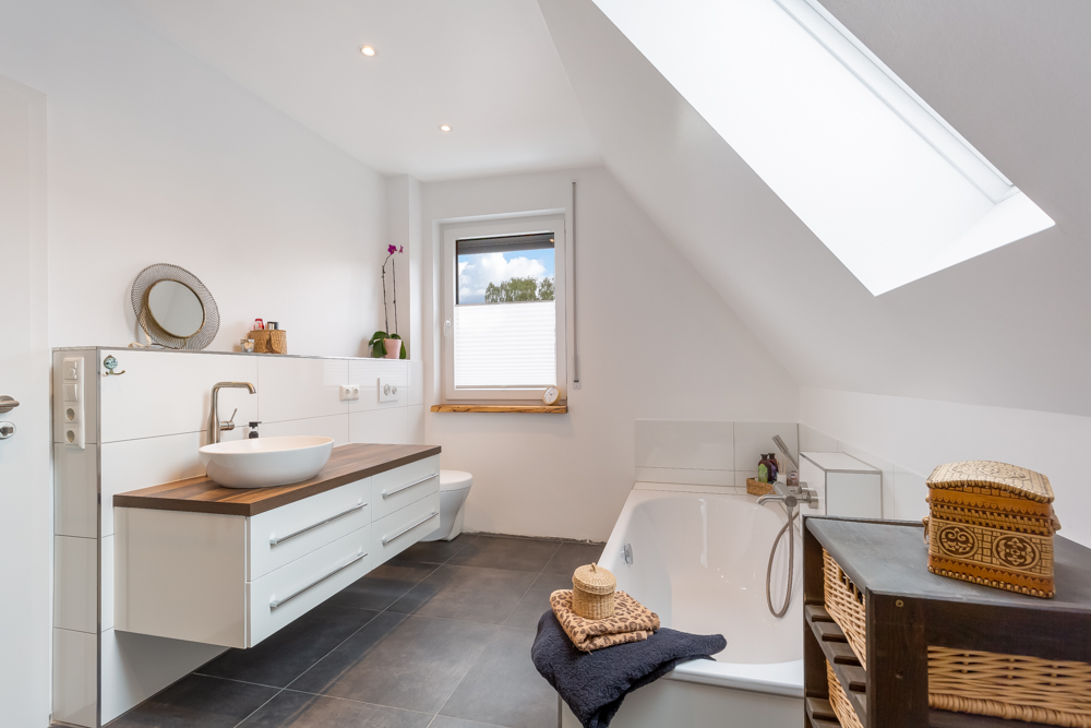 Modernes Badezimmer mit Badewanne, Waschbecken, Fenster und Dachfenster.