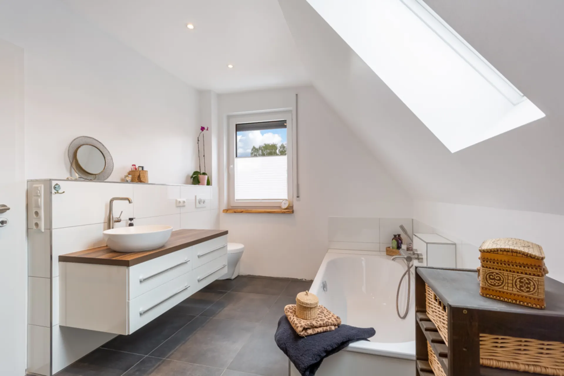 Modernes Badezimmer mit Badewanne, Waschbecken, Fenster und Dachfenster.