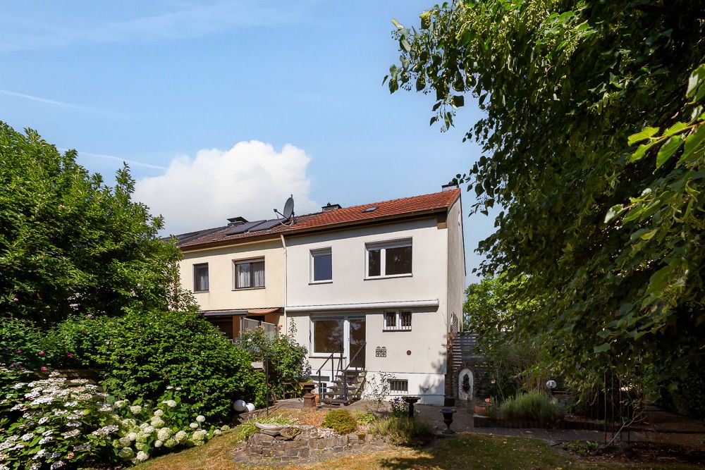 Rückseite eines Reihenhauses mit Garten und Bäumen im Vordergrund.
