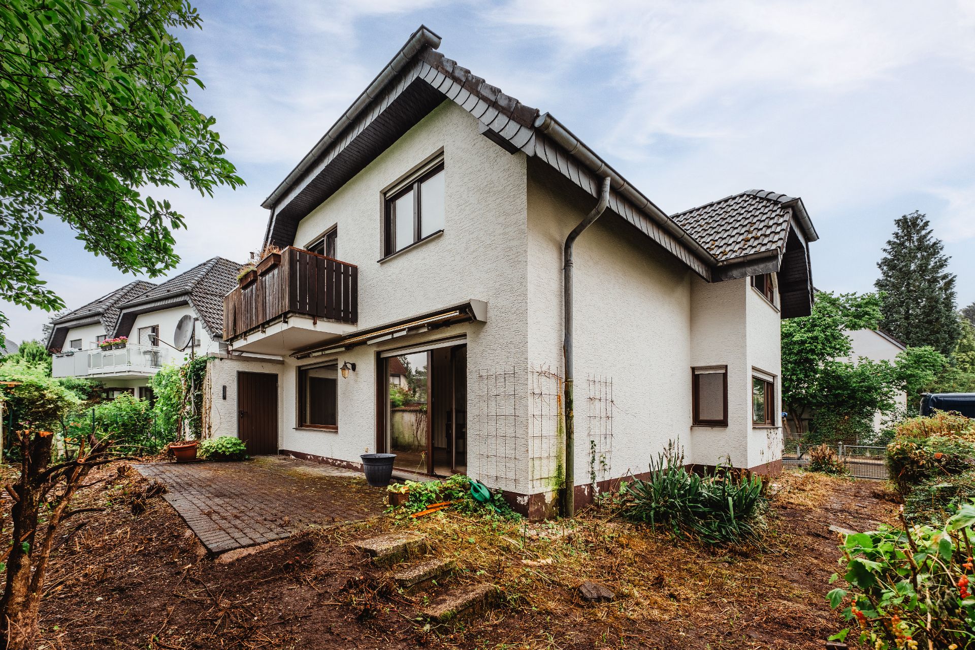 Zweistöckiges Wohnhaus mit Balkon und Garten, sichtbarer Eingang und Terrasse.