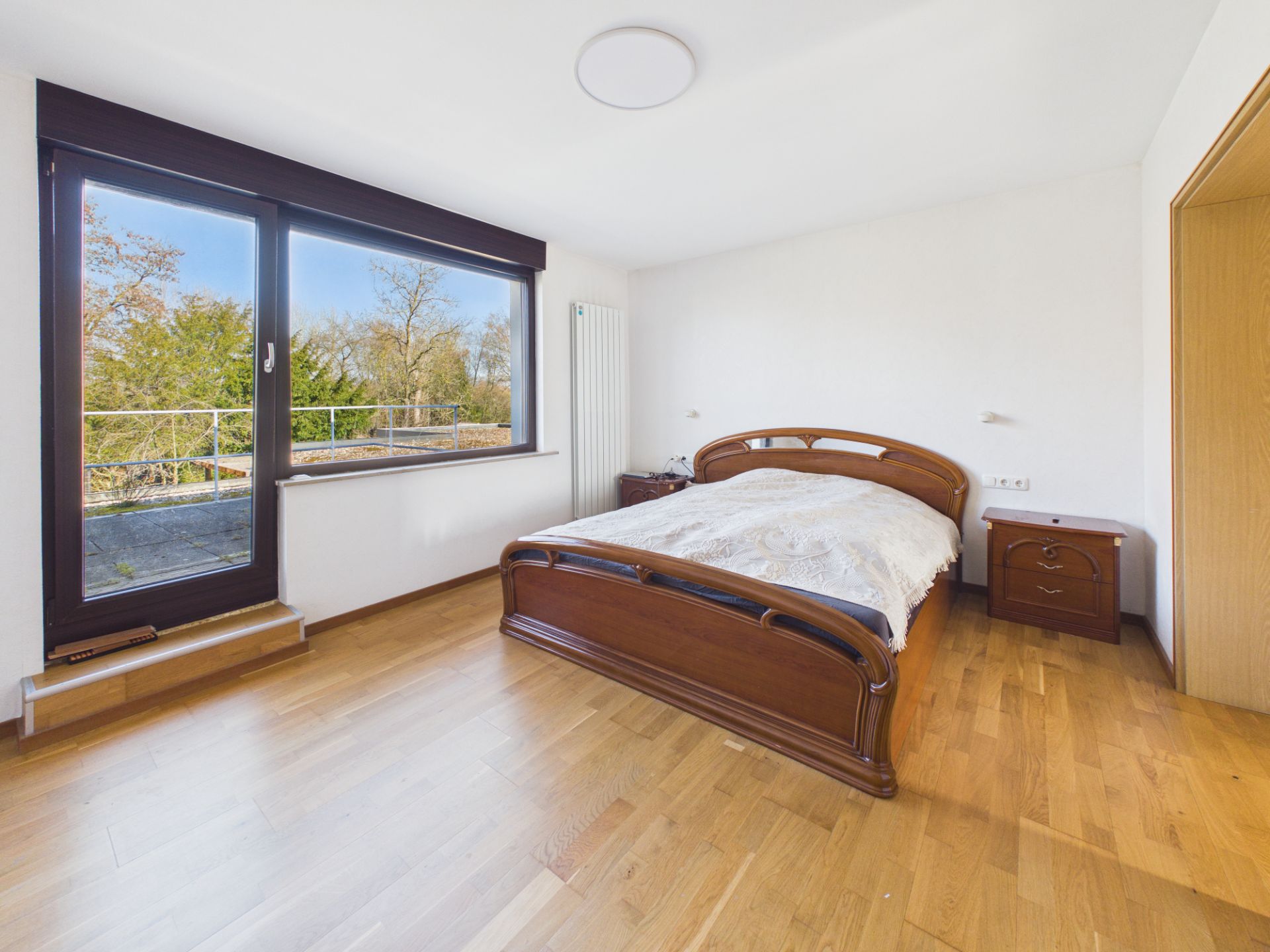 Helles Schlafzimmer mit Holzfußboden, großem Fenster, Doppelbett und Nachttischen.
