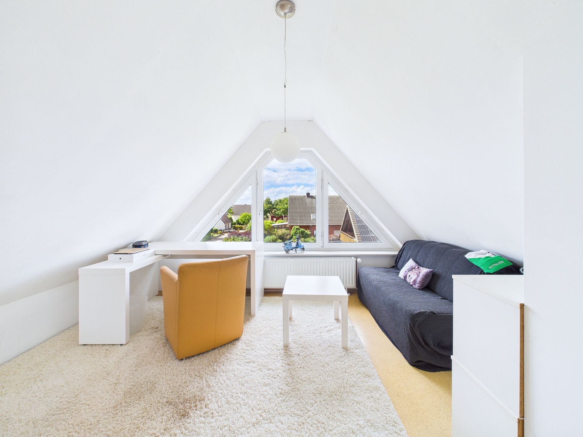 Helles Dachzimmer mit Schreibtisch, Sessel, Sofa und großen Fenstern.