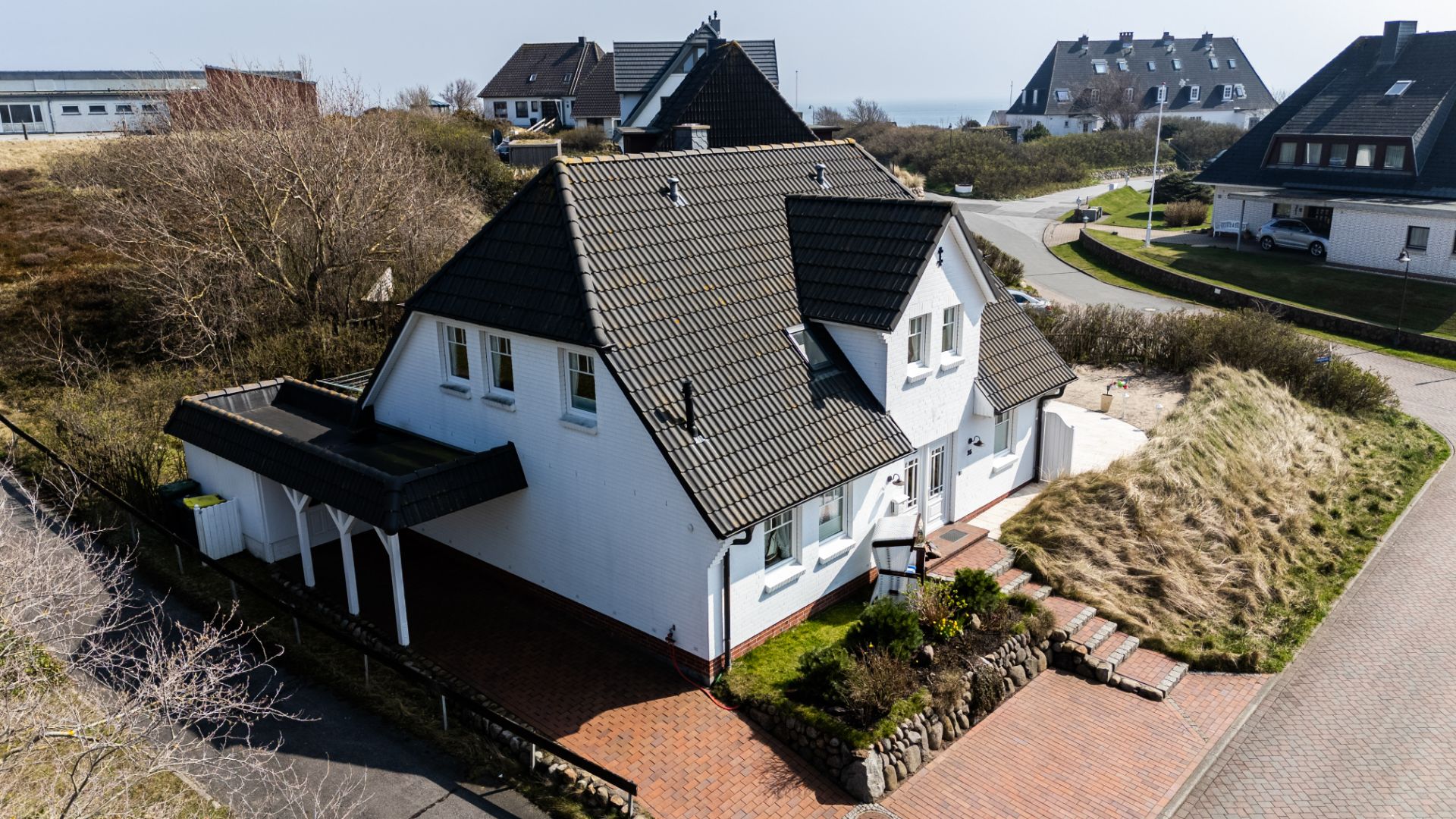Weißes Einfamilienhaus mit schwarzem Dach und Vorgarten in einer Wohnsiedlung.