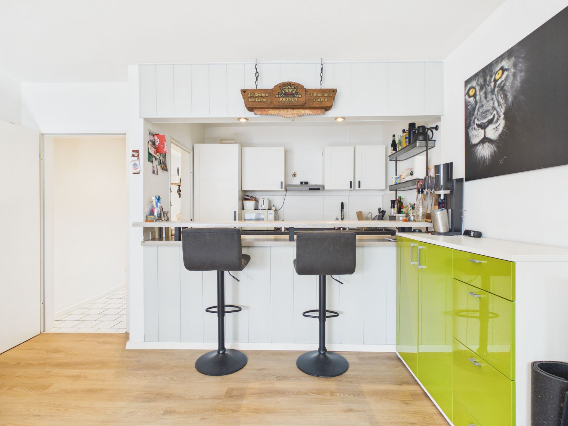 Moderne Küche mit Bartresen, zwei Barhockern und grünen Schränken, Löwenbild an der Wand.