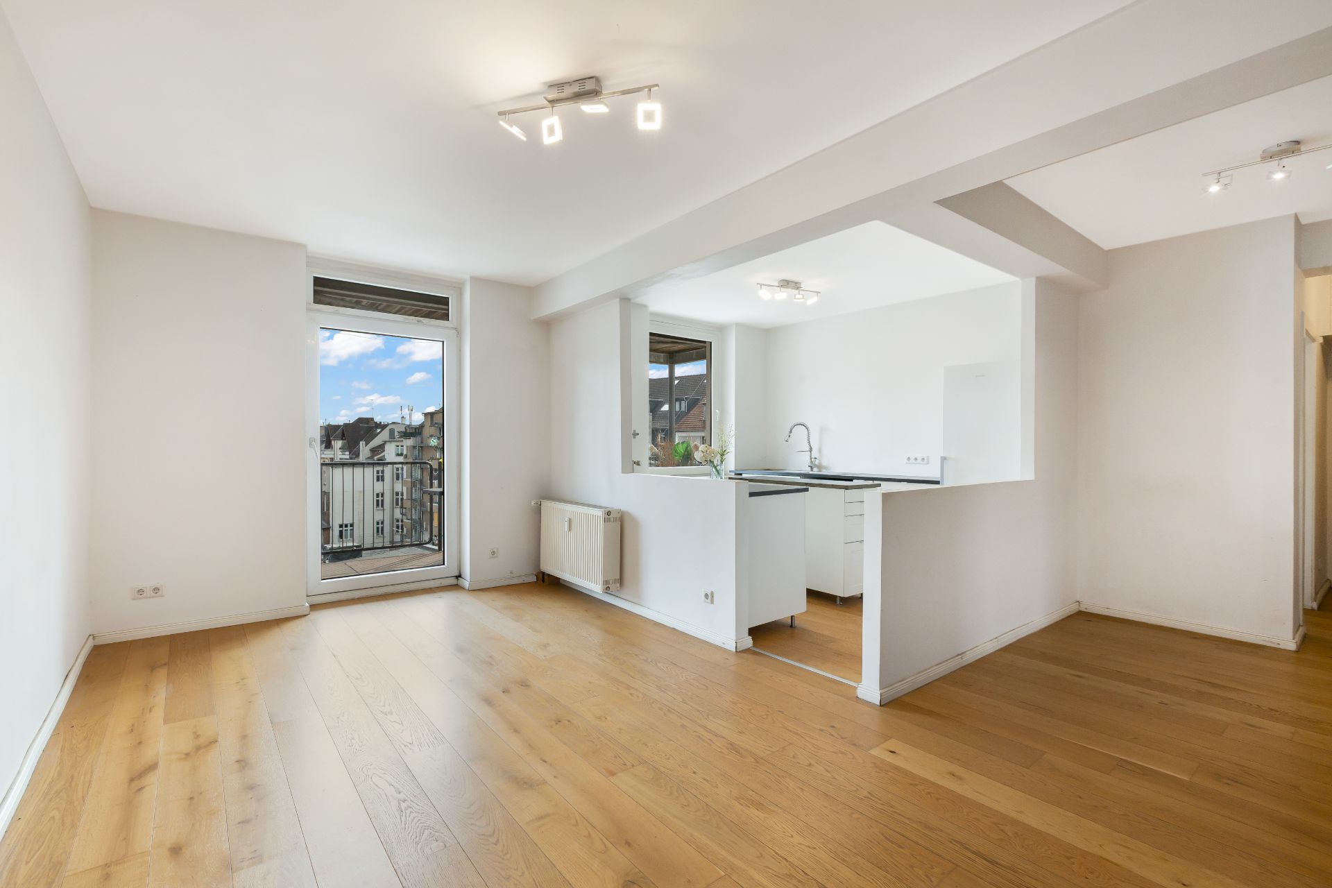 Helles Wohnzimmer mit Holzboden, Fenster und offener Küche.