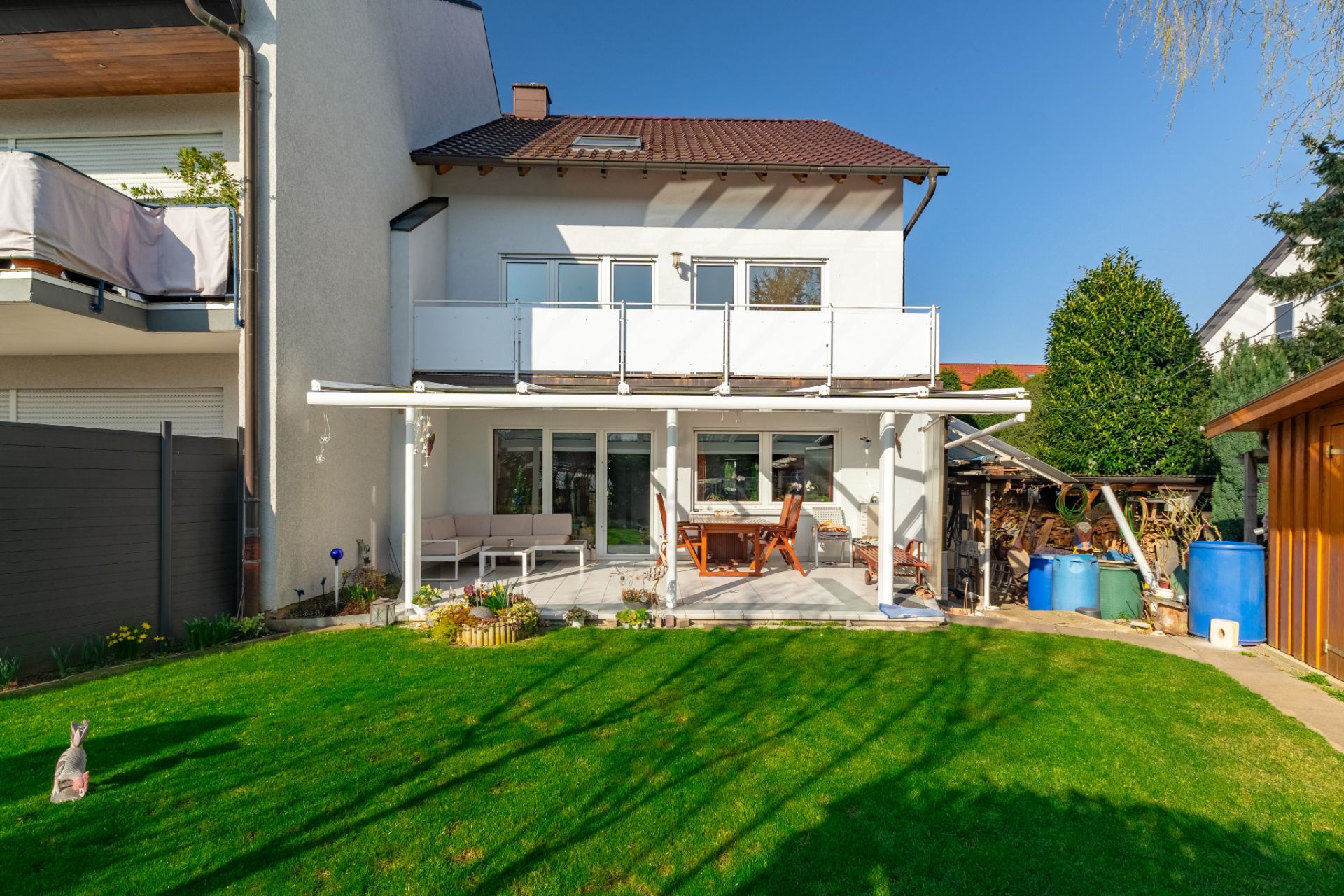Rückansicht eines Wohnhauses mit Terrasse, Gartenmöbeln und grünem Rasen.