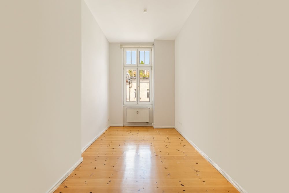 Heller, leerer Raum mit Holzboden und einem großen Fenster an der Stirnseite.