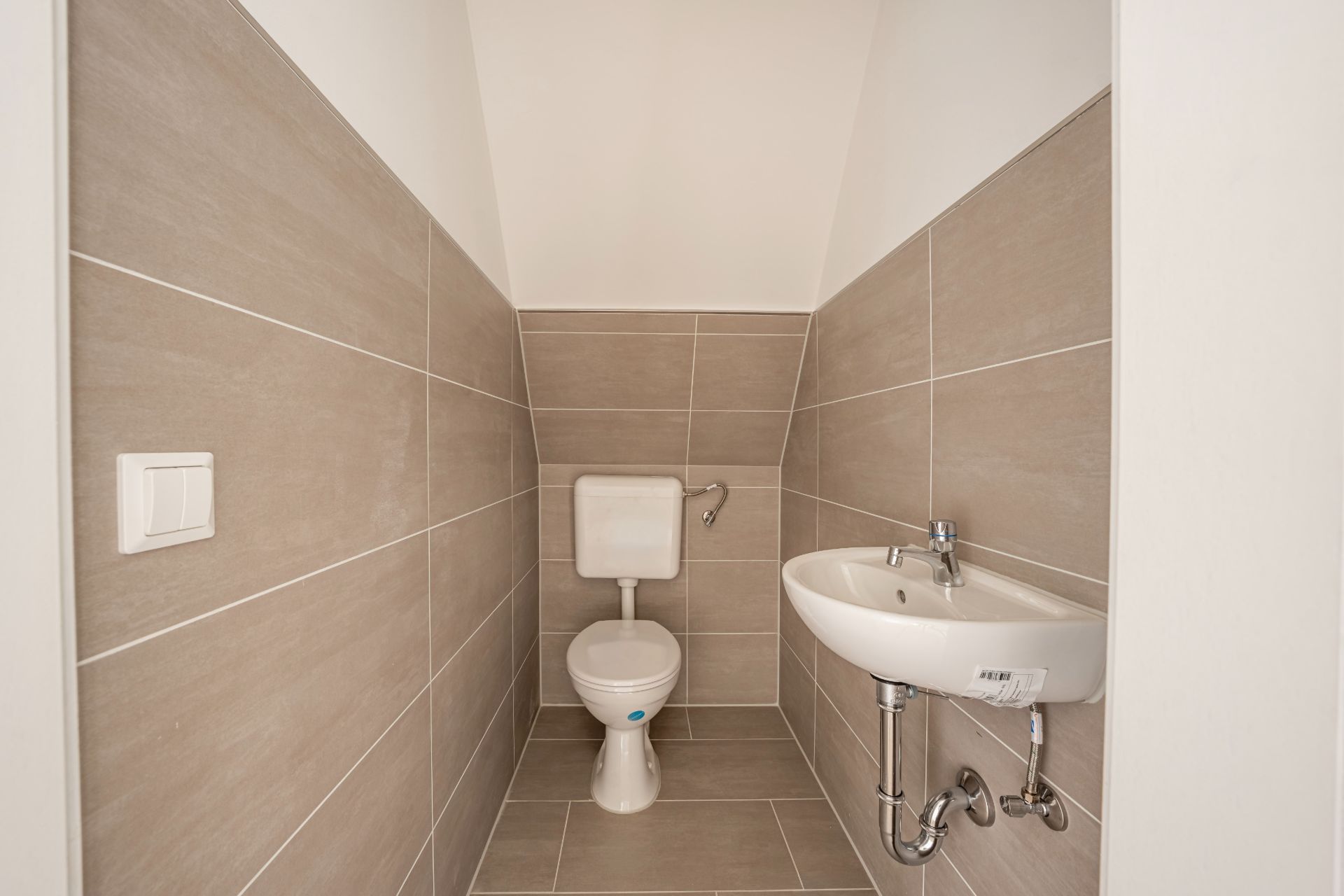 Kleines, gefliestes WC mit Toilette und Waschbecken.