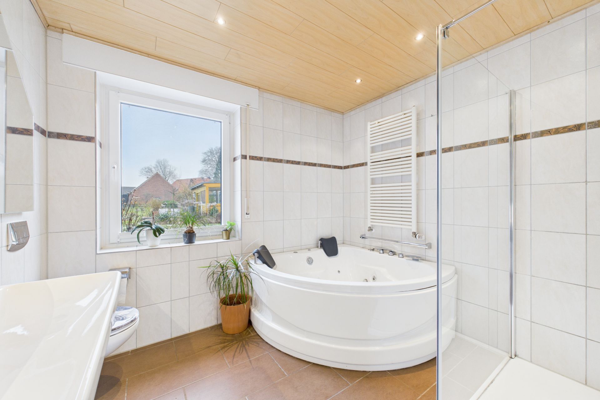 Modernes Badezimmer mit Eckbadewanne, Fenster, Pflanzen und Dusche.