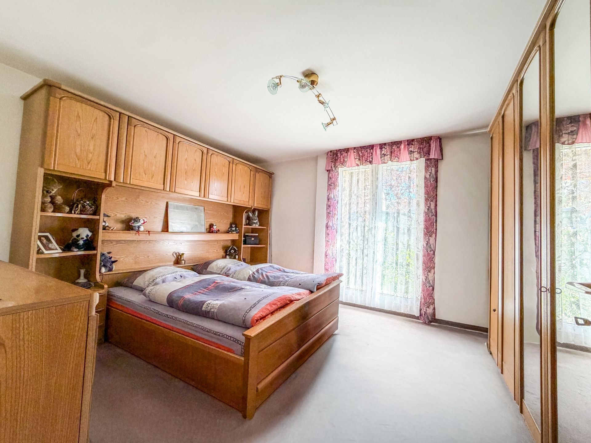 Helles Schlafzimmer mit Doppelbett, Holzschränken und Fenster mit Vorhängen.