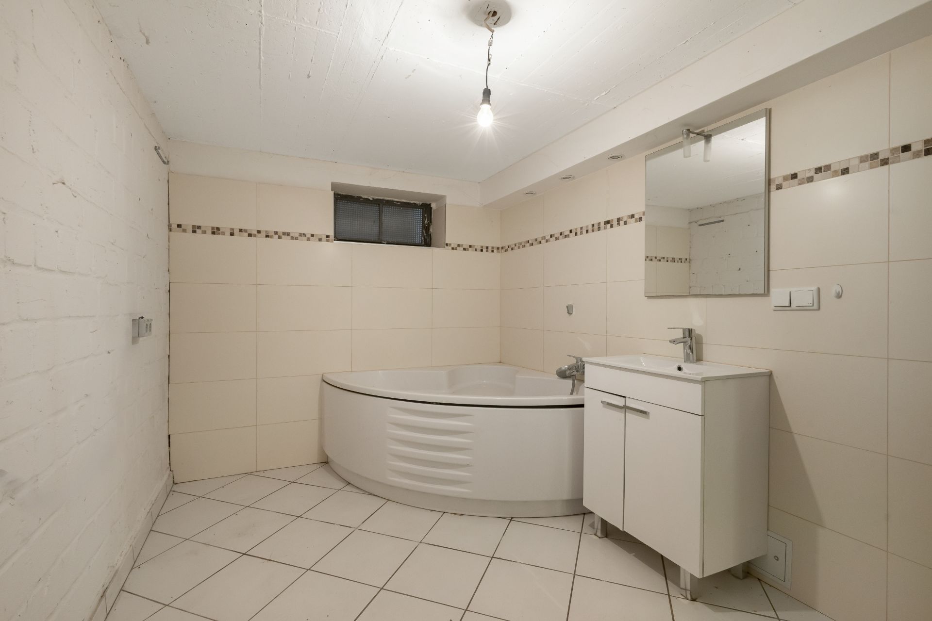 Helles Badezimmer mit Eckbadewanne, Waschbecken mit Spiegel und kleinem Fenster.