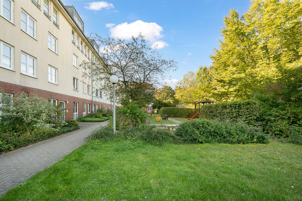 Wohnhaus mit Weg, Grünfläche, Bäumen und Kinderspielplatz mit Rutsche im Garten.
