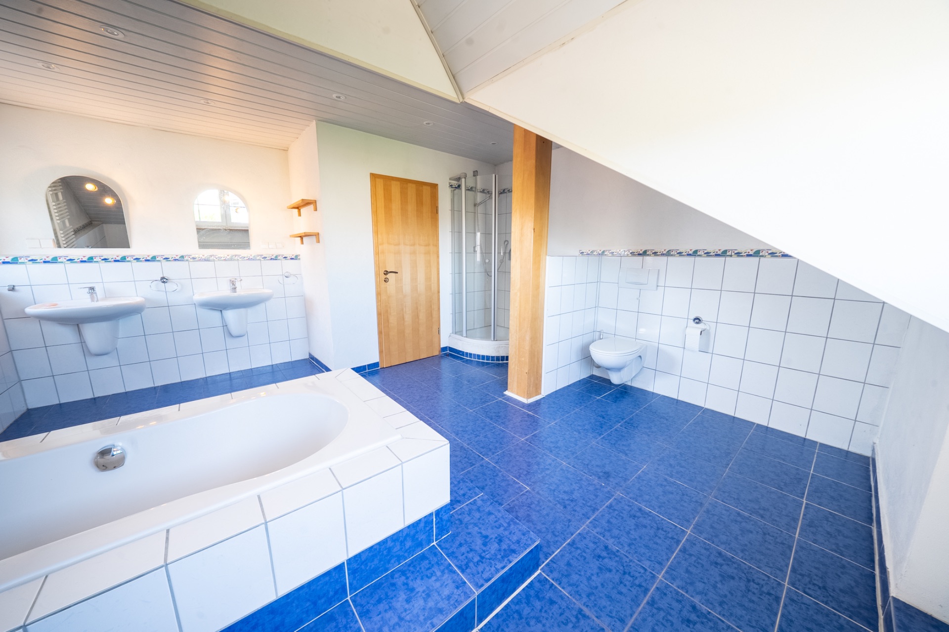Helles Badezimmer mit blauen Fliesen, Badewanne, zwei Waschbecken, Dusche und WC.