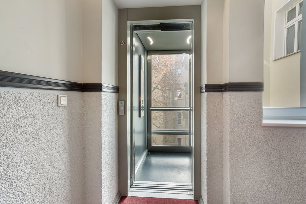 Geöffneter Aufzug in einem Wohnhausflur mit Blick nach draußen.