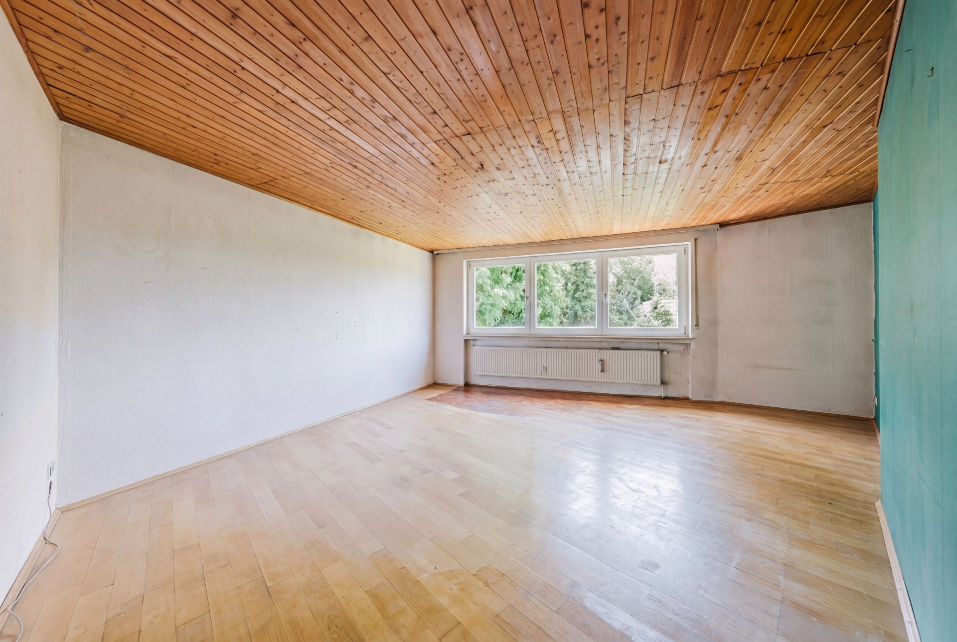 Leerer Raum mit Holzboden, Holzdecke und großer Fensterfront mit Blick auf Bäume.