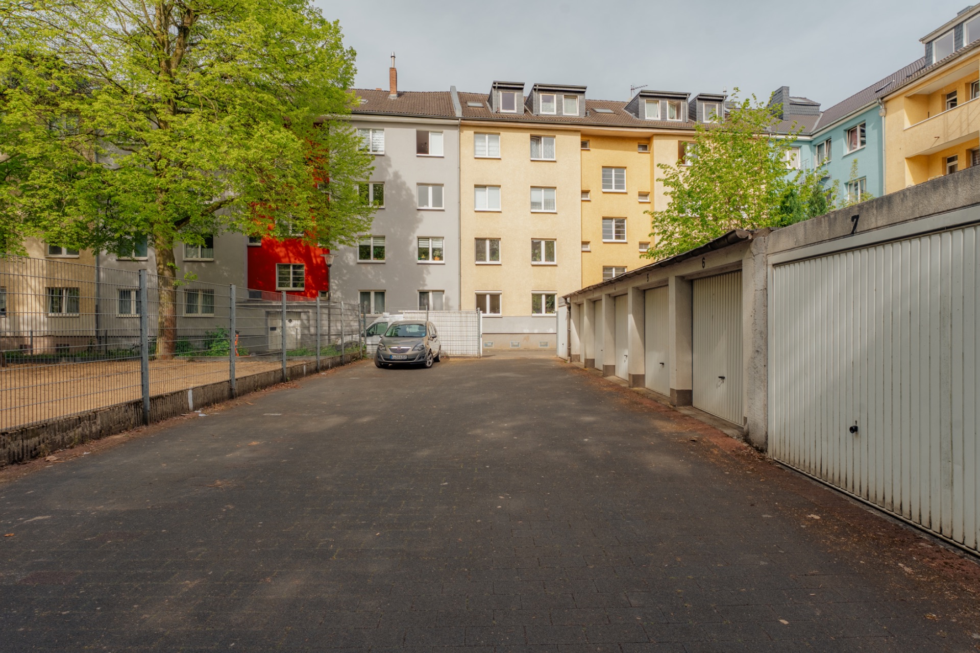 Ein Parkplatz mit Garagen und einem geparkten Auto vor mehrstöckigen Wohngebäuden.