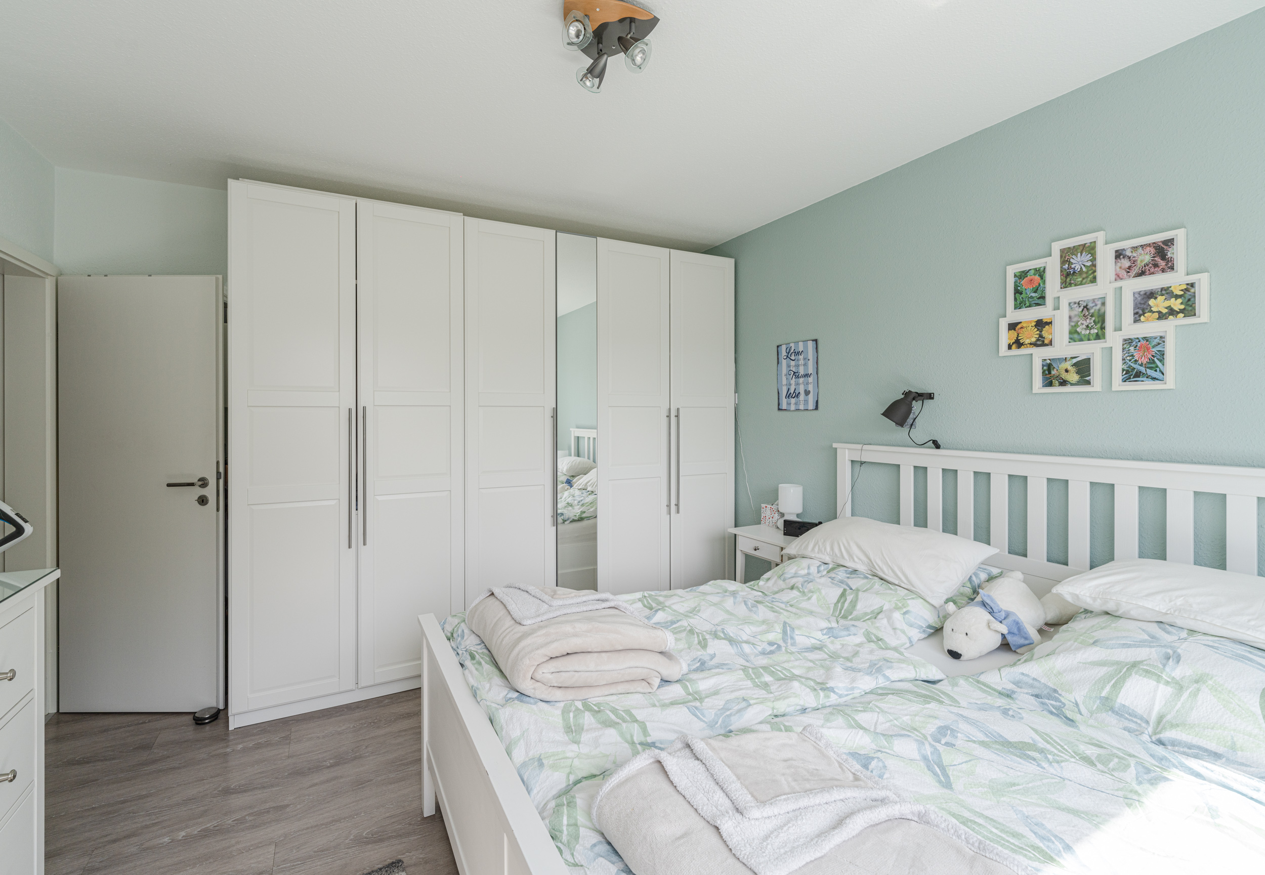 Helles Schlafzimmer mit Doppelbett, weißen Schränken und dekorativen Bildern an der Wand.