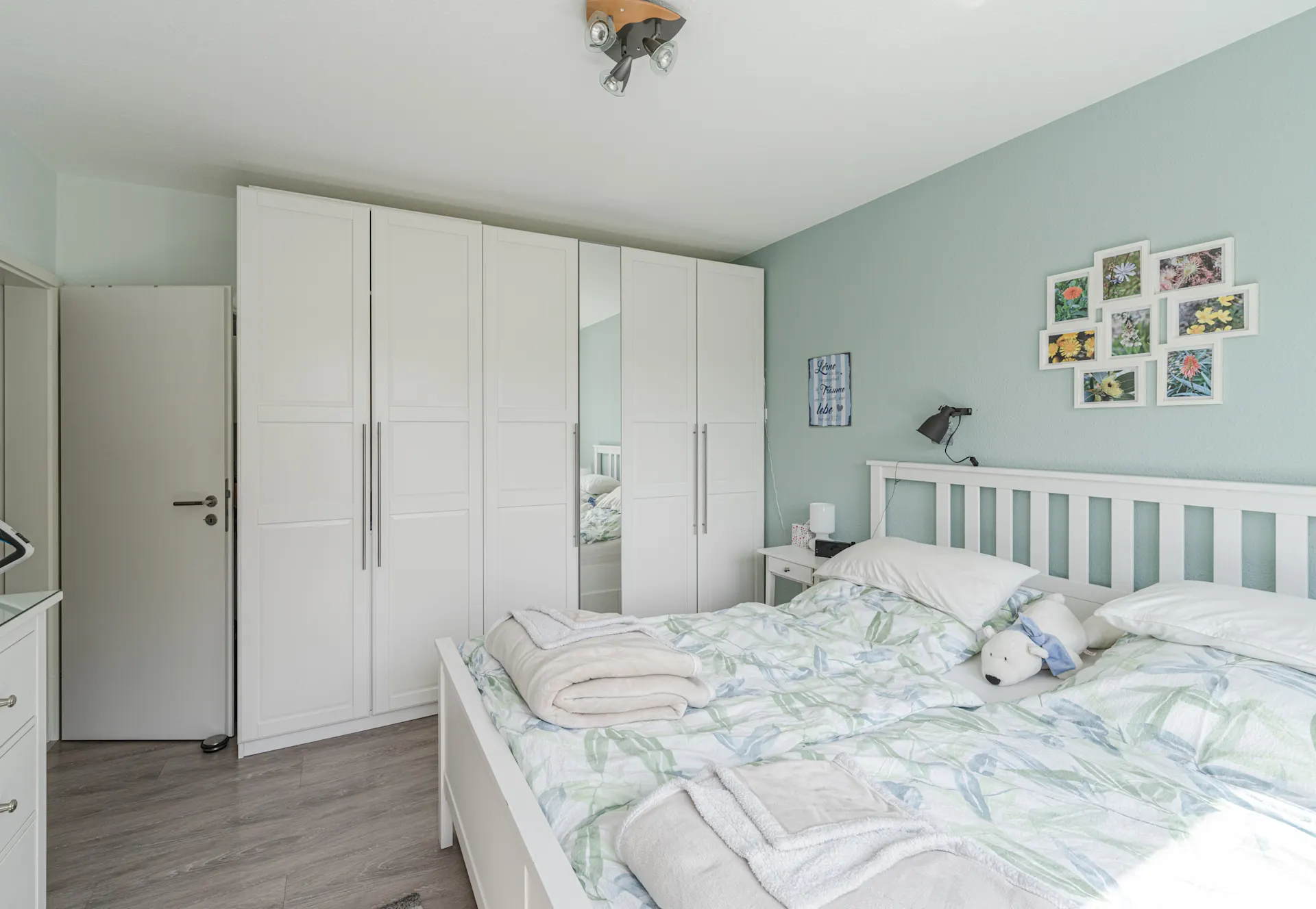 Helles Schlafzimmer mit Doppelbett, weißen Schränken und dekorativen Bildern an der Wand.