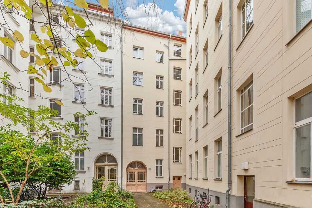 Innenhof eines Wohnhauses mit Pflanzen, mehreren Fenstern und Fahrrädern.