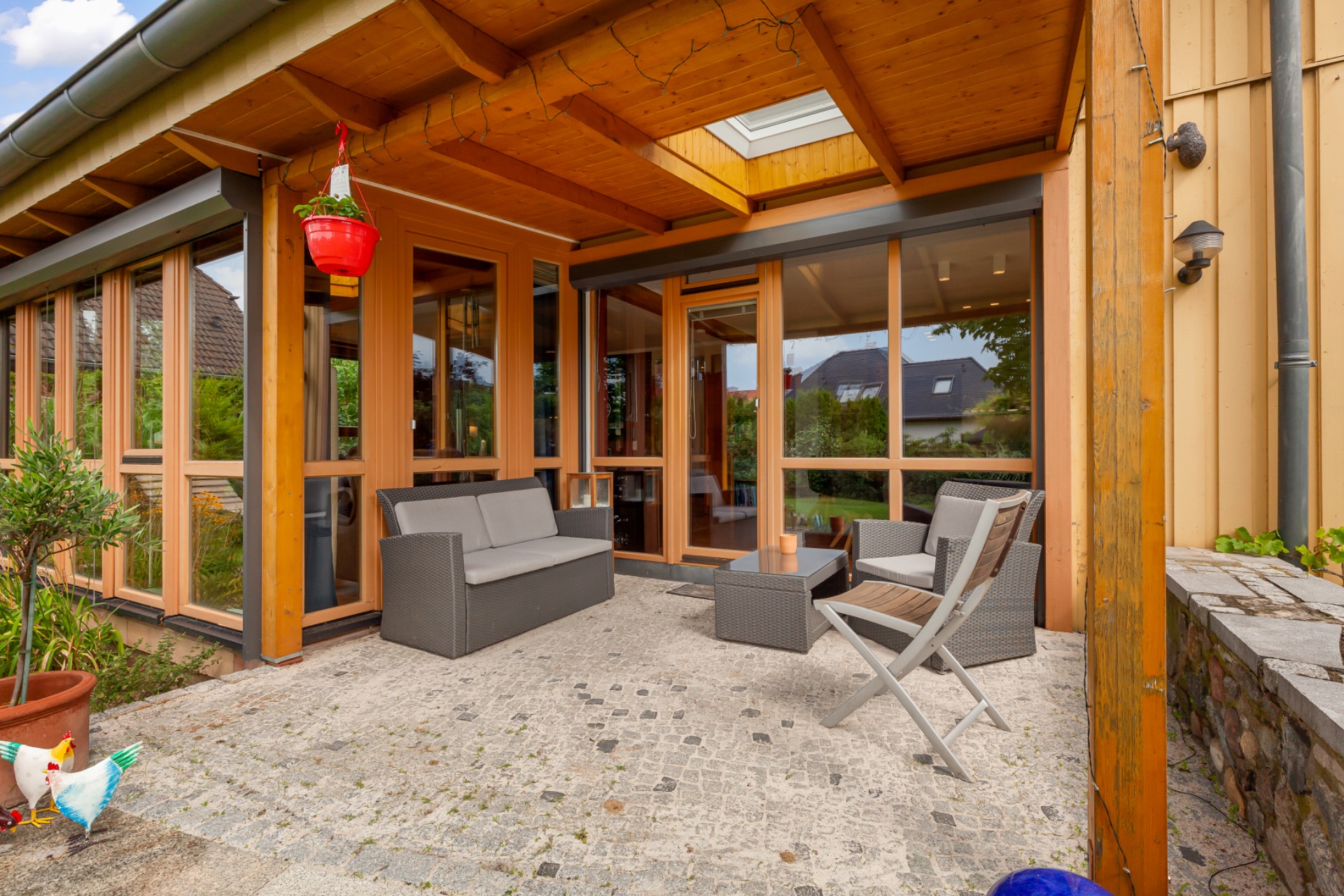 Überdachte Terrasse mit Sitzmöbeln vor einem modernen Haus mit vielen Fenstern.