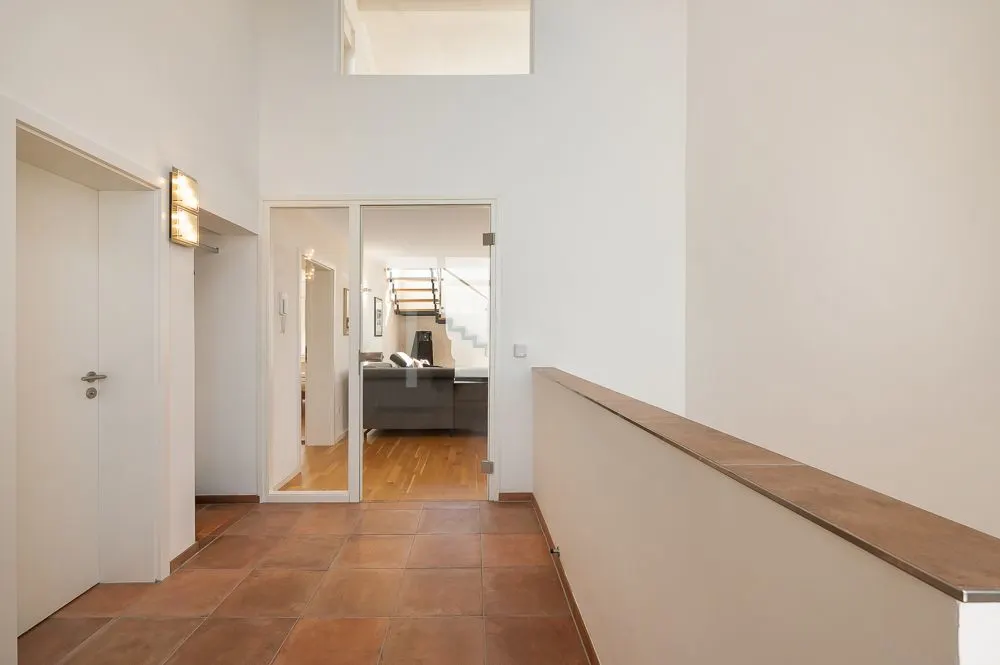 Heller Flur mit Terrakottafliesen, einer Glastür und Blick ins Wohnzimmer mit Treppe.