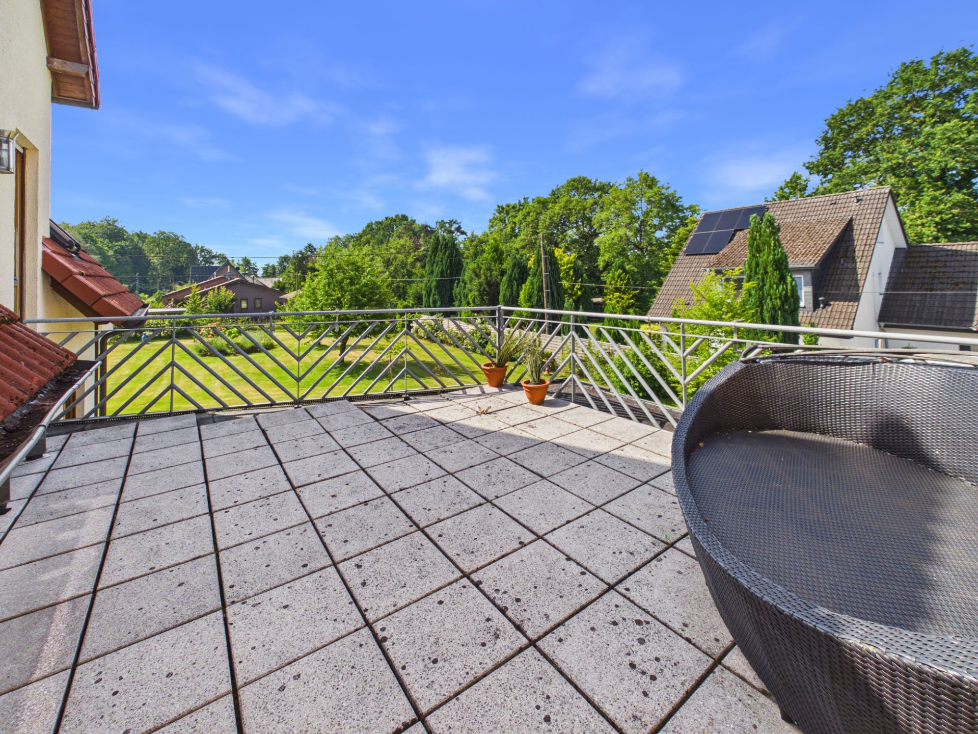 Große Terrasse mit Fliesenboden, Rundsofa, Pflanzen und Blick auf Garten und Nachbarhäuser.