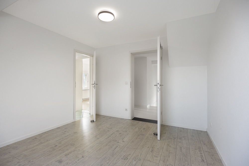 Heller, leerer Raum mit Holzboden, weißen Wänden und zwei offenen Türen.
