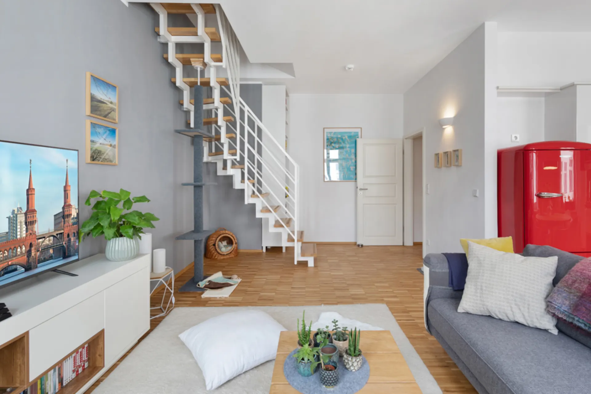Modernes Wohnzimmer mit grauem Sofa, rotem Kühlschrank und offener Treppe.