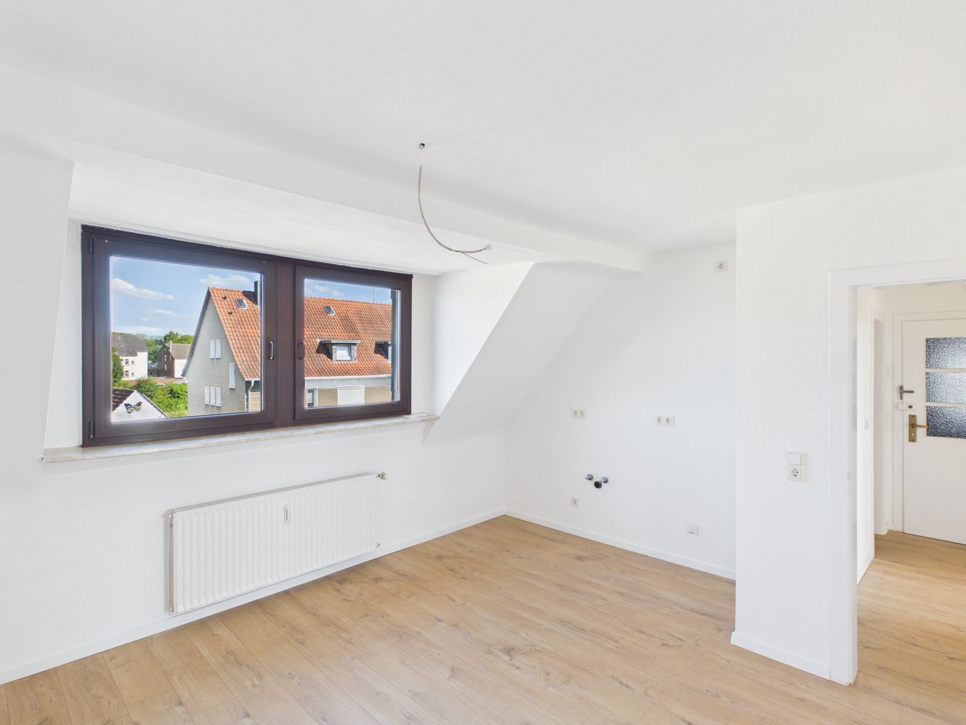 Helles Zimmer mit Dachfenster, Holzboden und weiß gestrichenen Wänden.
