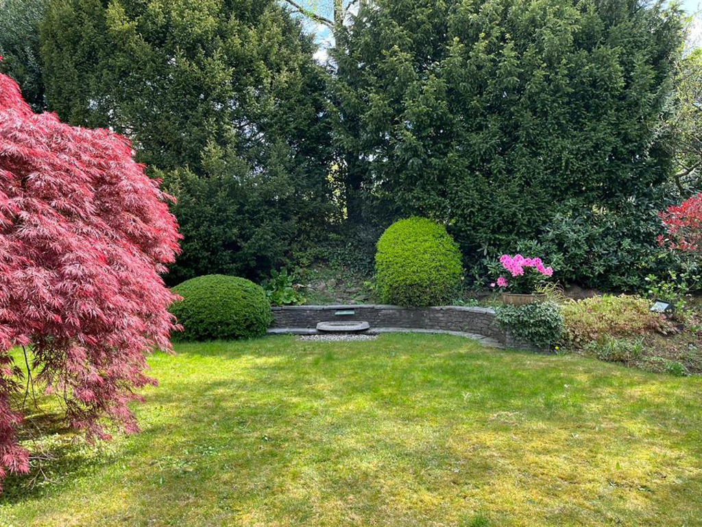 Gepflegter Garten mit grünem Rasen, Sträuchern und einem kleinen Steinsitzplatz.