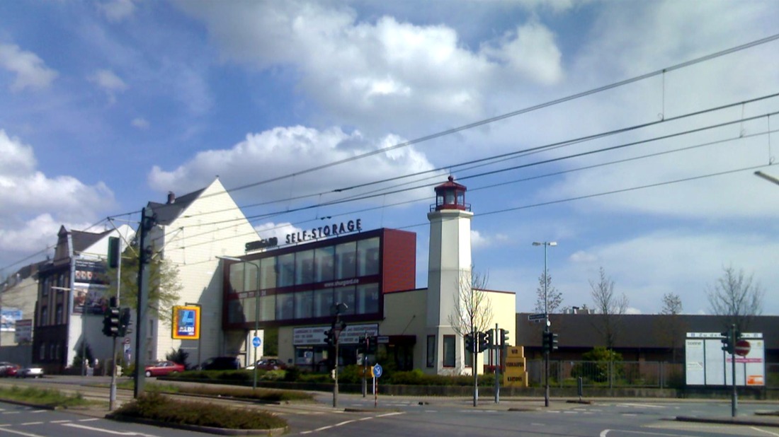 Gebäude mit Aufschrift 'Self-Storage' und Leuchtturm an einer Straßenecke, Ampeln im Vordergrund.