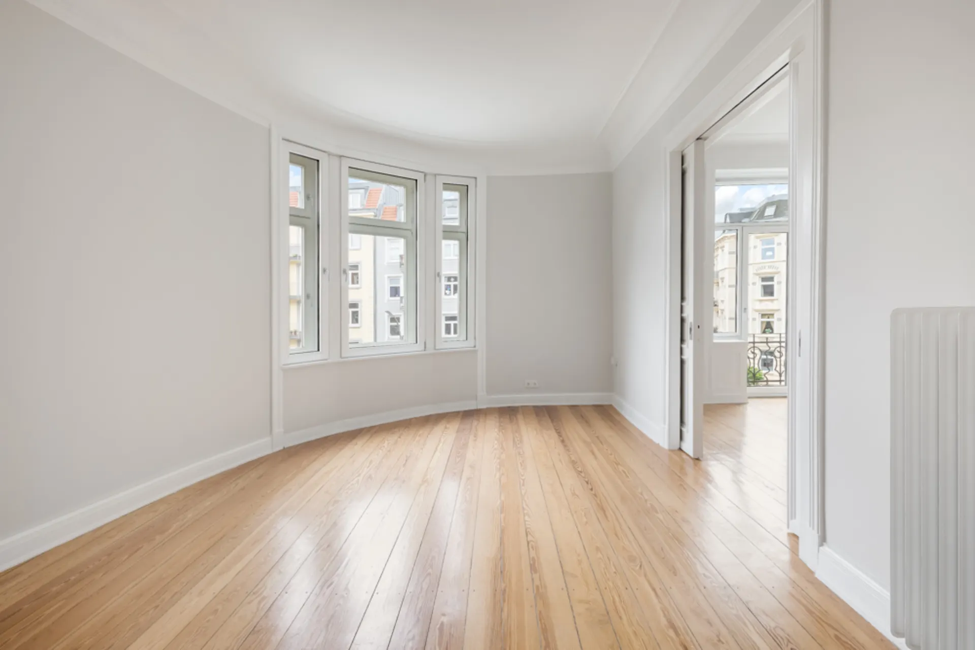 Heller Raum mit Holzboden, Erkerfenstern und Durchgang zu weiterem Zimmer.