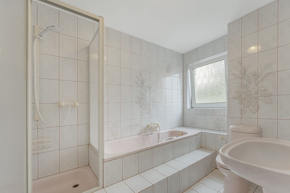 Helles Badezimmer mit Dusche, Badewanne, Waschbecken, Toilette und Fenster.