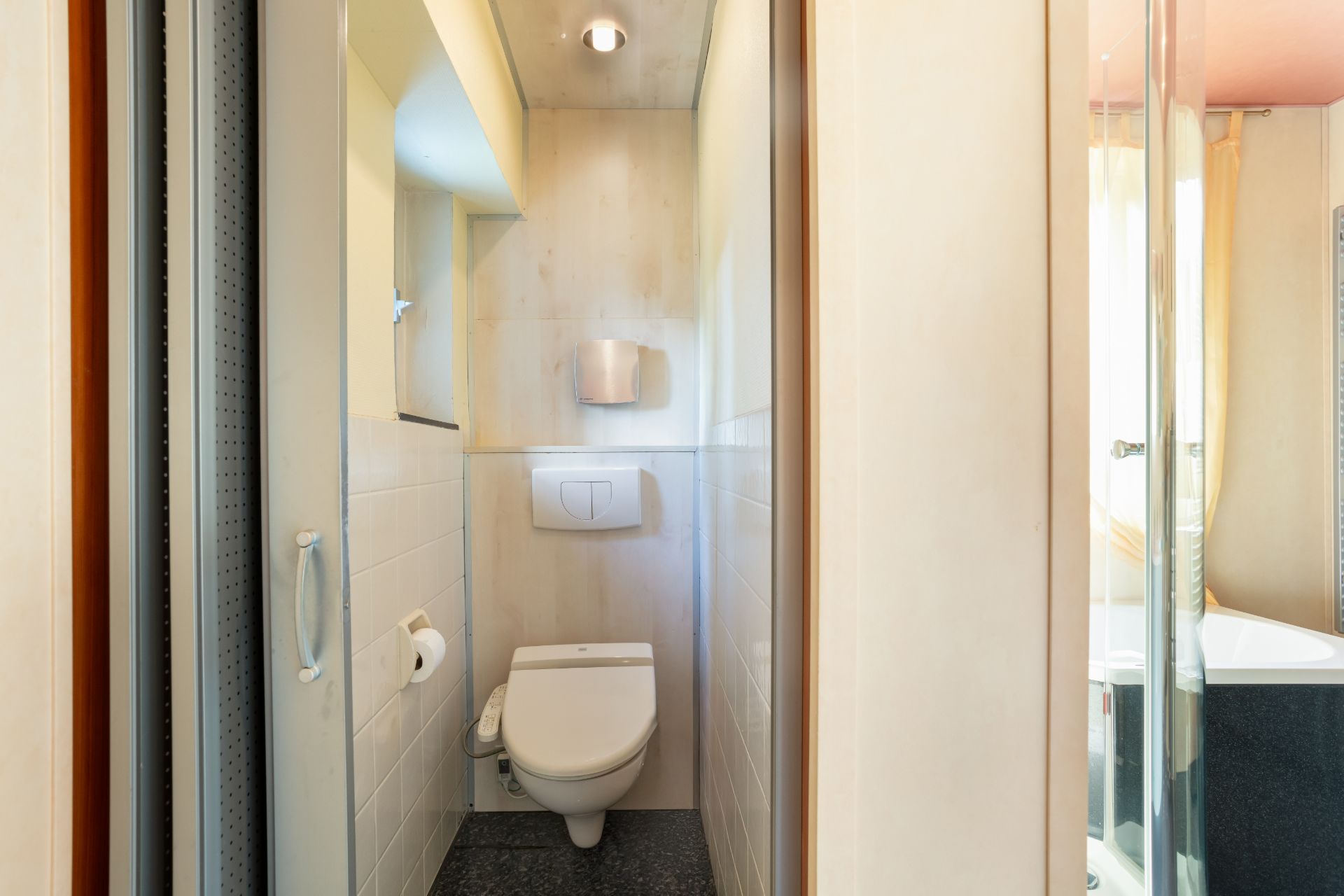Kleines Badezimmer mit Toilette, Toilettenpapierhalter und kleinem Fenster.